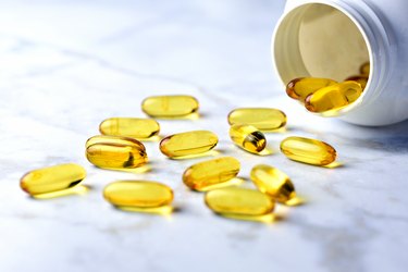 a close up photo of yellow vitamin D supplements spilling out of an open bottle onto a marble countertop